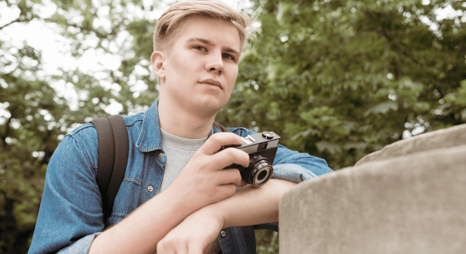 Young man leaning against a railing with a camera in his hand. 