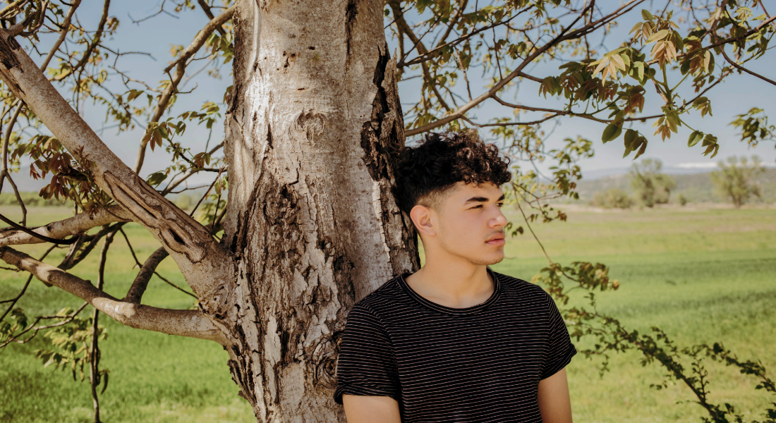 young man outside leaning against a tree