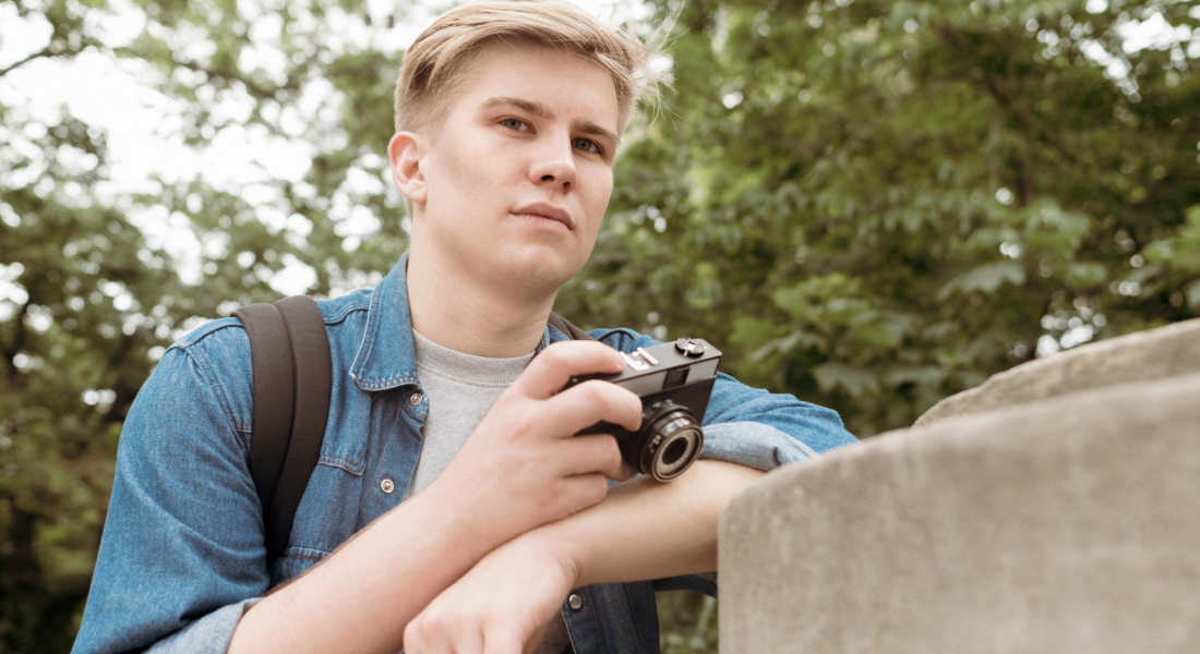 Young man leaning against a railing with a camera in his hand. 